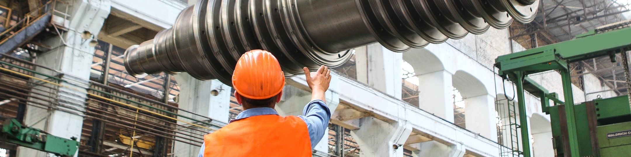 Man in orange safety vest guides machinery on crane